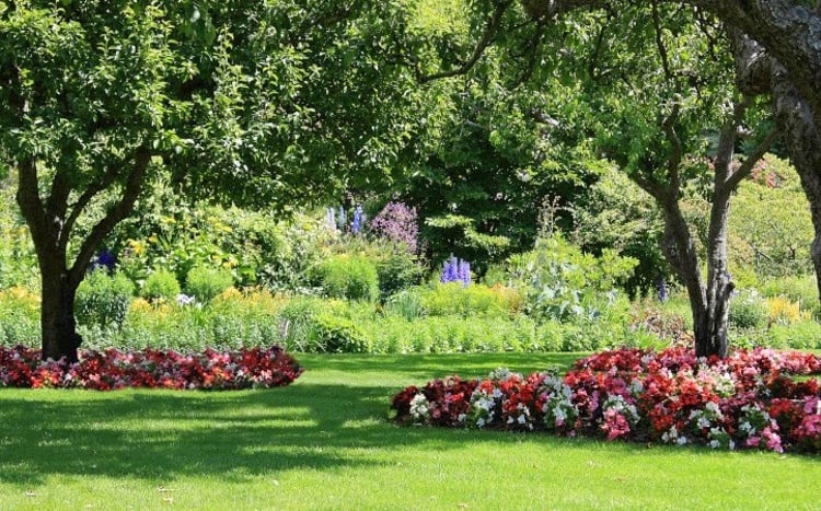 Lush landscaping with green grass, large green plants and trees, and red, white, and pink flowers.